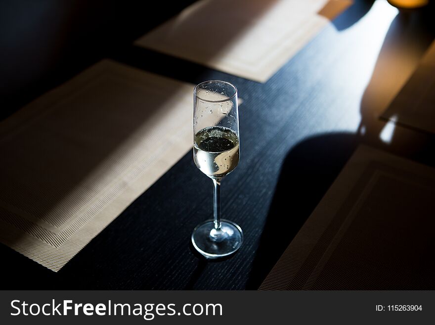 A glass of champagne shitoit on a dark wooden table in the setting sun