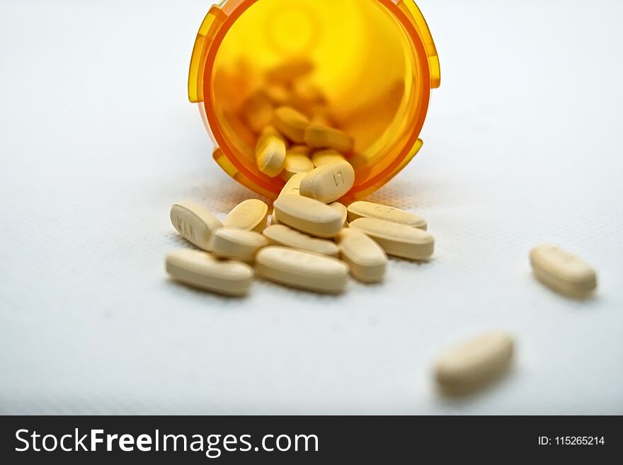 Medicine bottle toppled over with pills spilling out the end onto a table. Medicine bottle toppled over with pills spilling out the end onto a table.