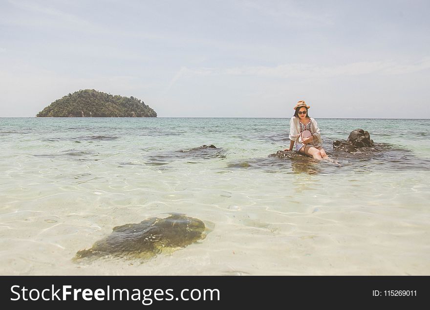 Woman Wearing White Top Sitting on Brown Rock on Body of Water during