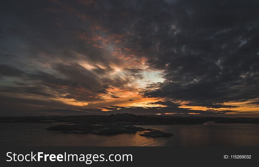 Silhouette of Island Under Grey Clouds during Golden Hour