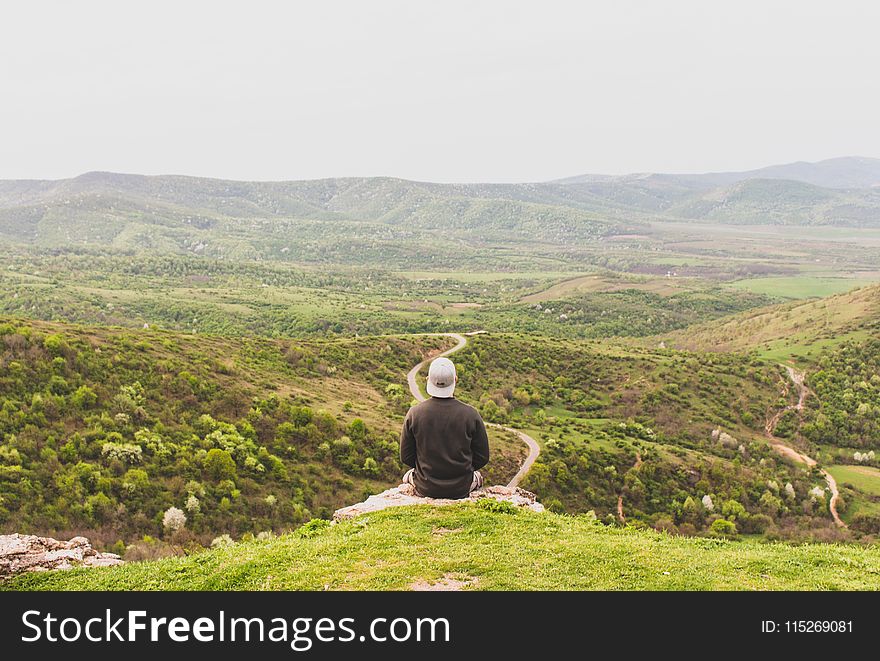 Man Sitting on Mountain Facing Forest Field