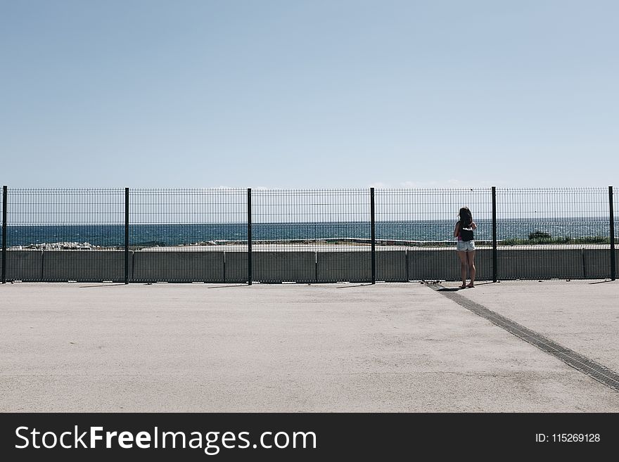 Woman Standing Near Fence and Body of Water