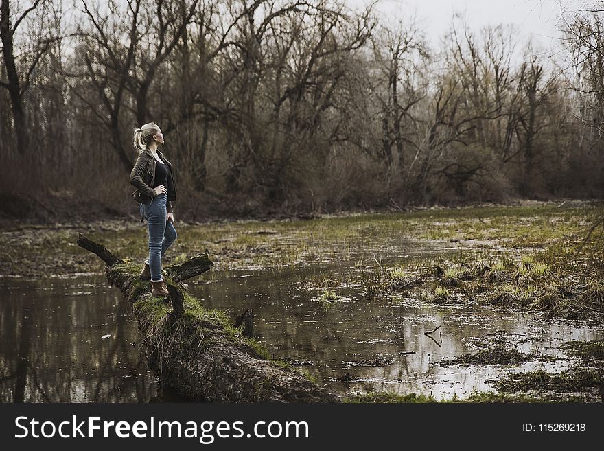 Woman Standing on Driftwood Above Body of Water