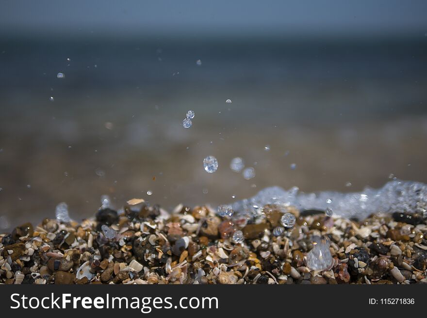 Flying sprays and drops of water. wet sea pebbles on a summer beach pebbles. summer beach. blue sky