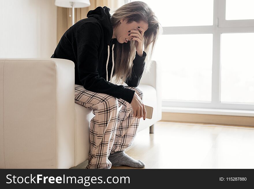 Depressed woman sitting in couch with mobile phone in hand