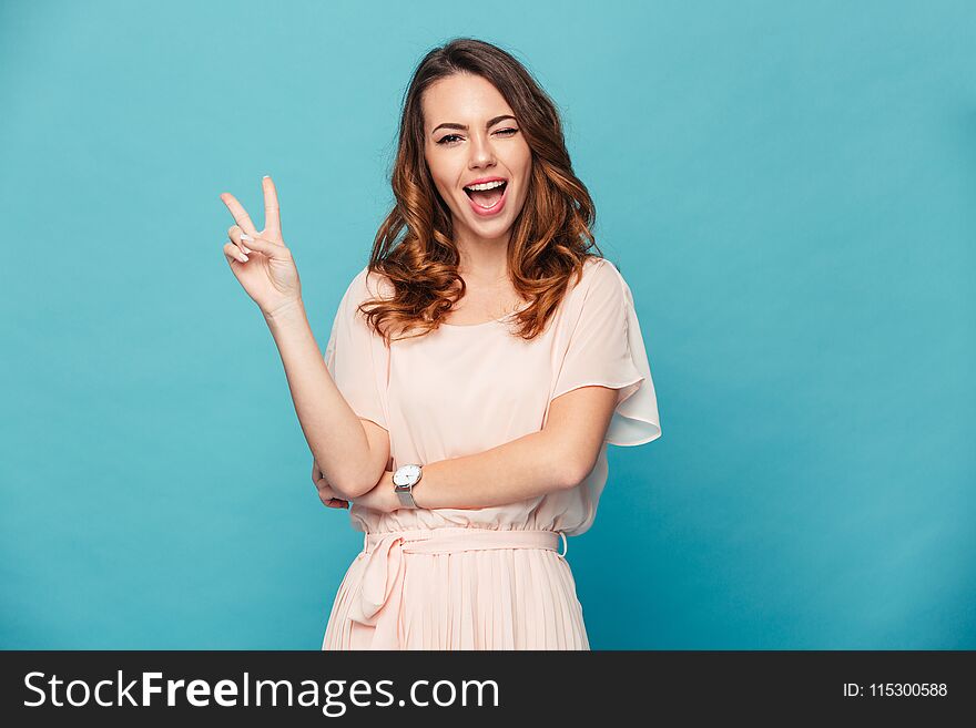 Image of cute young lady standing isolated over blue background. Looking camera showing peace gesture. Image of cute young lady standing isolated over blue background. Looking camera showing peace gesture.