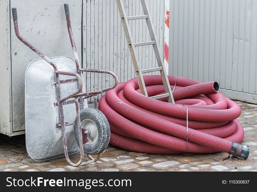 Construction site with wheelbarrow ladder and plastic pipe, Germany