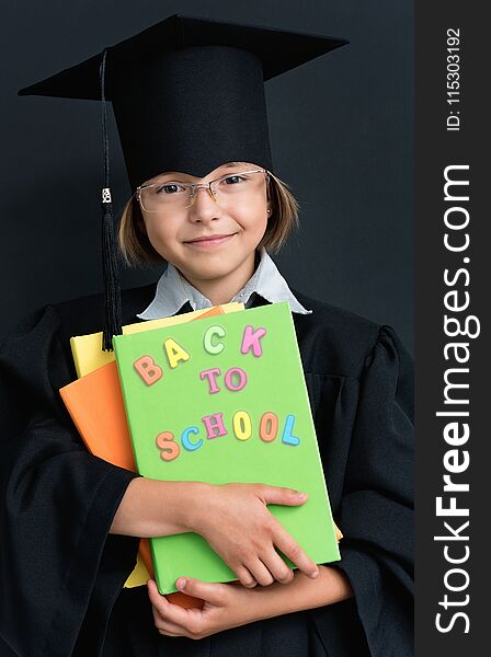 Portrait of graduate little girl student in black graduation gown with hat and books, on white background. Child back to school and educational concept. Portrait of graduate little girl student in black graduation gown with hat and books, on white background. Child back to school and educational concept.