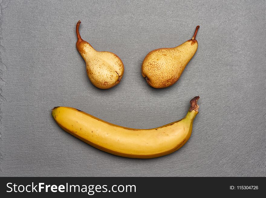 Scary smile made of two pears and banana lying on gray slate background, top view