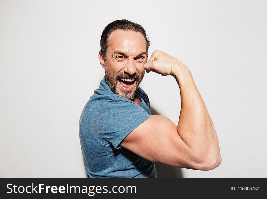 Portrait of a happy mature man dressed in t-shirt showing biceps isolated over white background