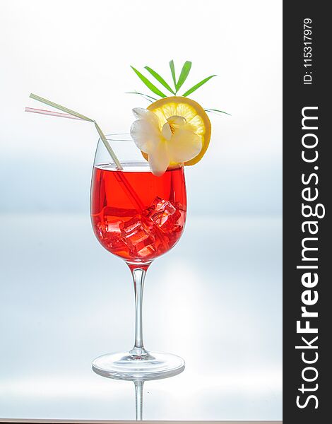 Colorful summer tropical cocktail in a glass with ice cubes, couple of straws, , slice of lemon and a tropical plants.