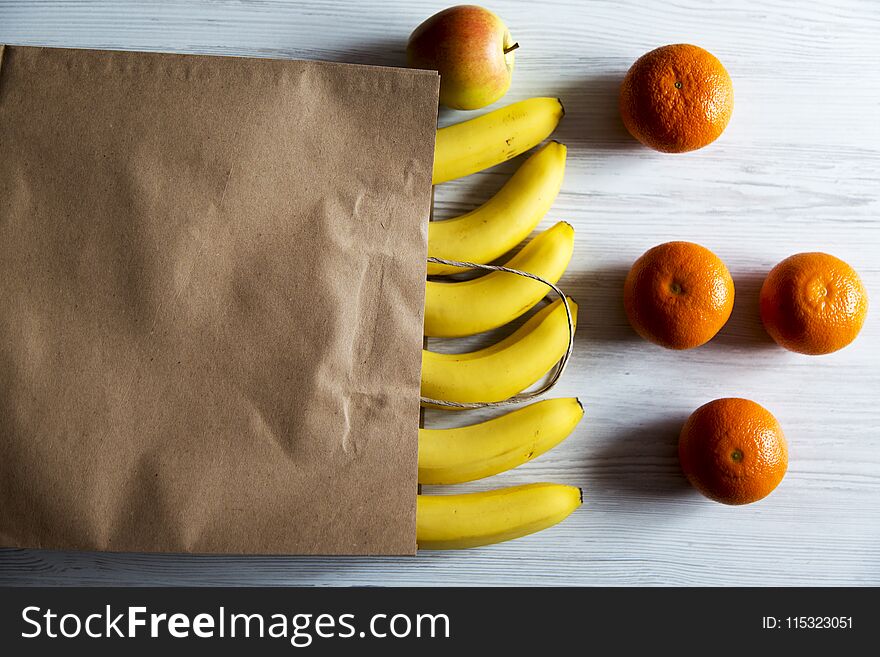 Paper bag of different fruits on white wooden background. Flat lay