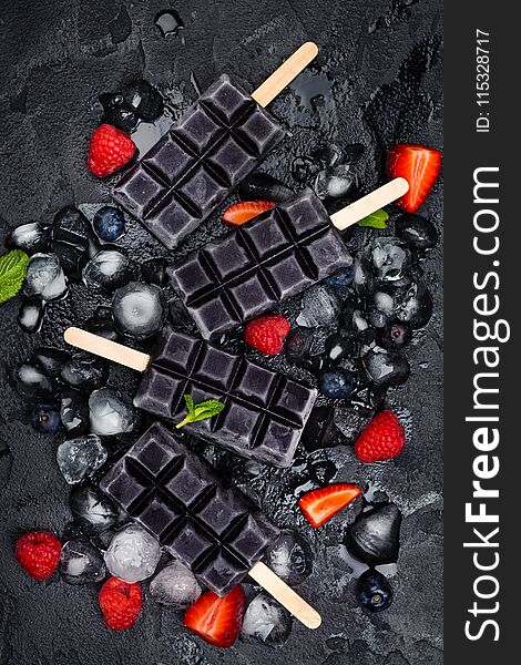 Trendy black charcoal ice cream popsicles with berries on stone background. Copy space