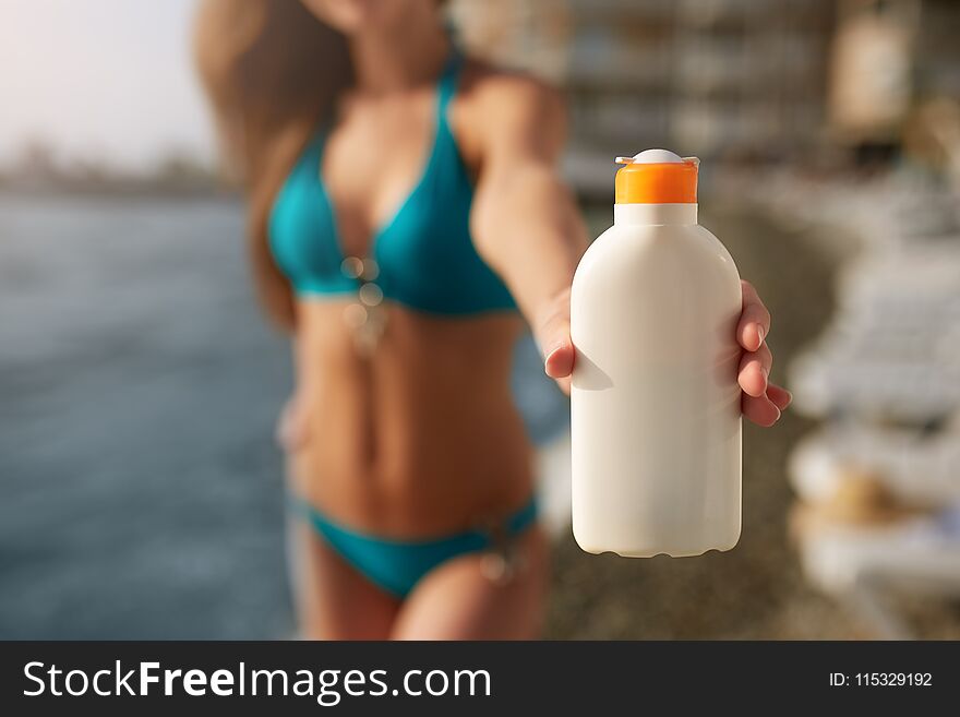 Happy Woman Shows The Suntan Or Sunscreen Cream White Bottle Over The Blurred Beach Background. Tanned Slim Girl Wearing