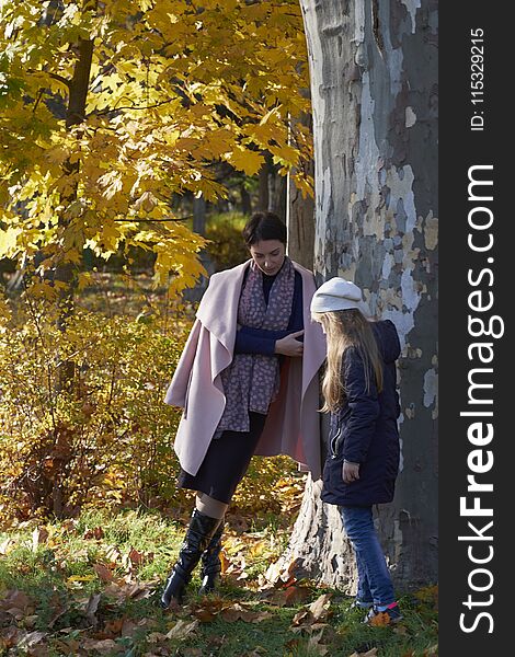 Mother and little girl hiding behind a tree in a park in autumn. Tree of Platanus