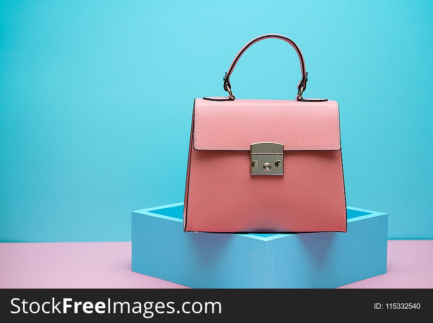 Coral leather female bag on the blue decorative stand on the pink surface on the cyan background in the studio. Closeup. Horizontal. Coral leather female bag on the blue decorative stand on the pink surface on the cyan background in the studio. Closeup. Horizontal.