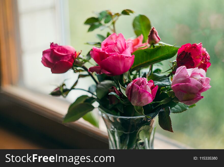 Homemade roses. Bouquet in a crystal vase on a wooden window. The concept of quiet and cozy village life, gardening and environmen