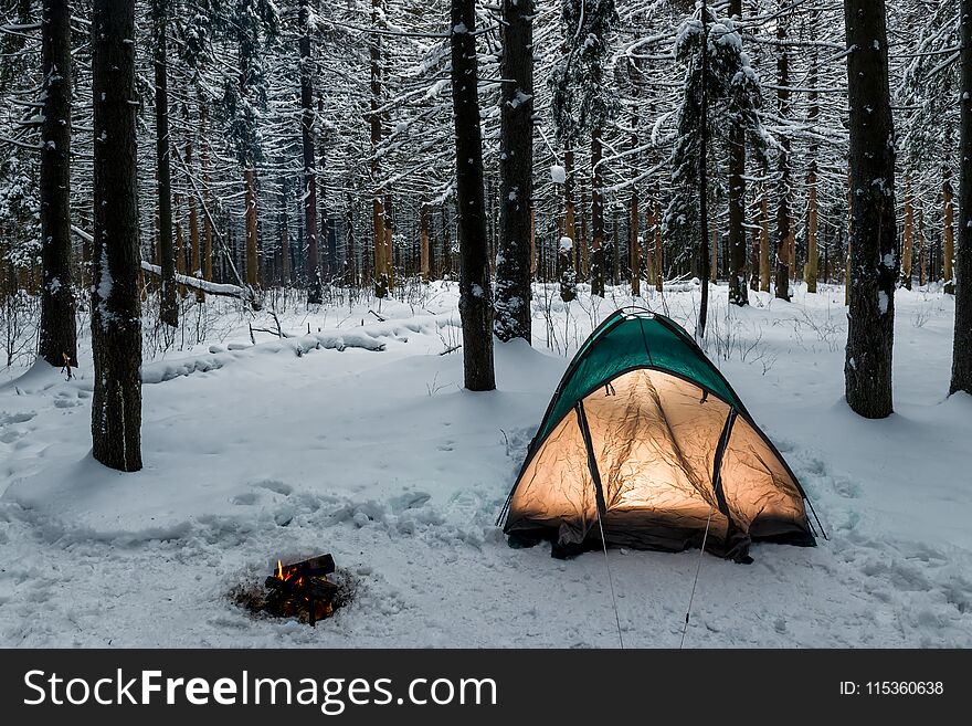 Tent in the winter forest on a hike, near a burning fire