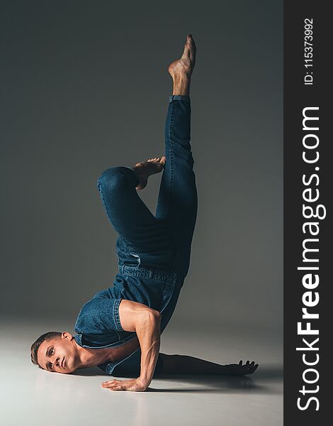 the guy is dancing, the pose of the leg is up, face to the floor, hands are lying on the floor, on a faded background in a denim suit. sport, tired, sad, broken,broken, doll.