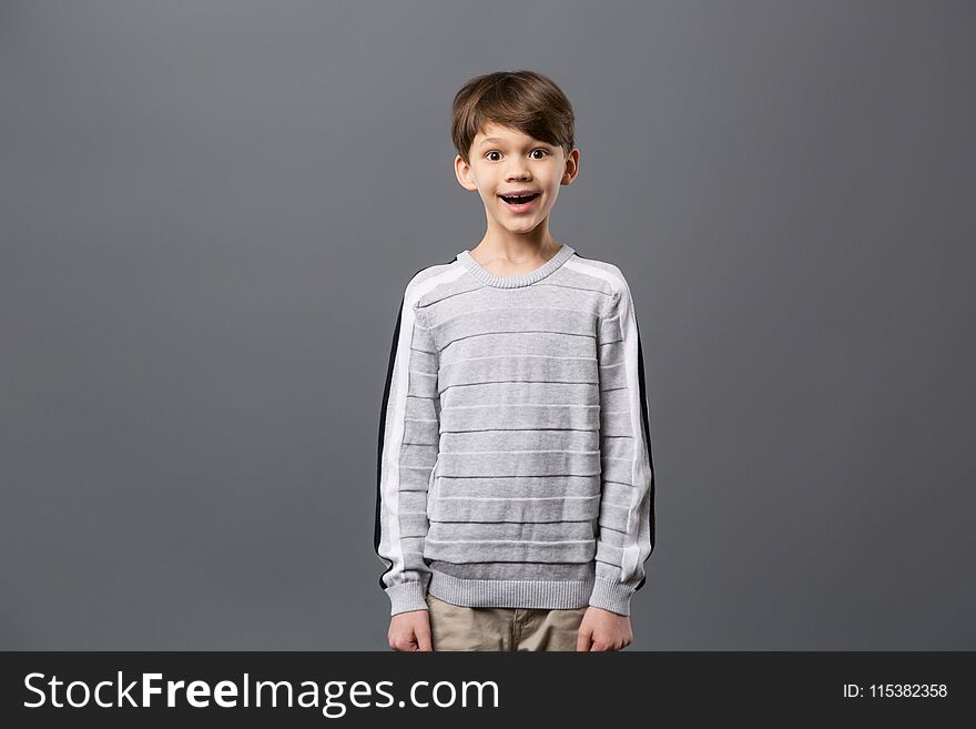 Emotional child. Happy excited boy standing against grey background and looking at you. Emotional child. Happy excited boy standing against grey background and looking at you