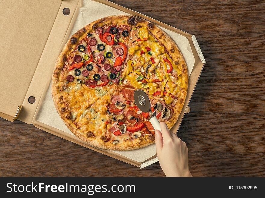 The girl`s hands cut a huge pizza in a box. Four pizzas in one