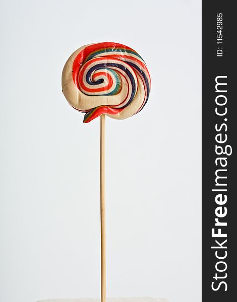 A colorful lollipop on white background supported on a polystyrene white cube. A colorful lollipop on white background supported on a polystyrene white cube