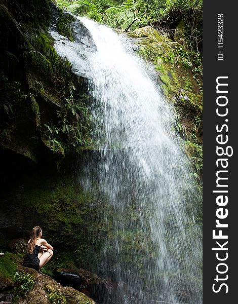 Photo of Woman Sitting on Rock Facing the Waterfalls