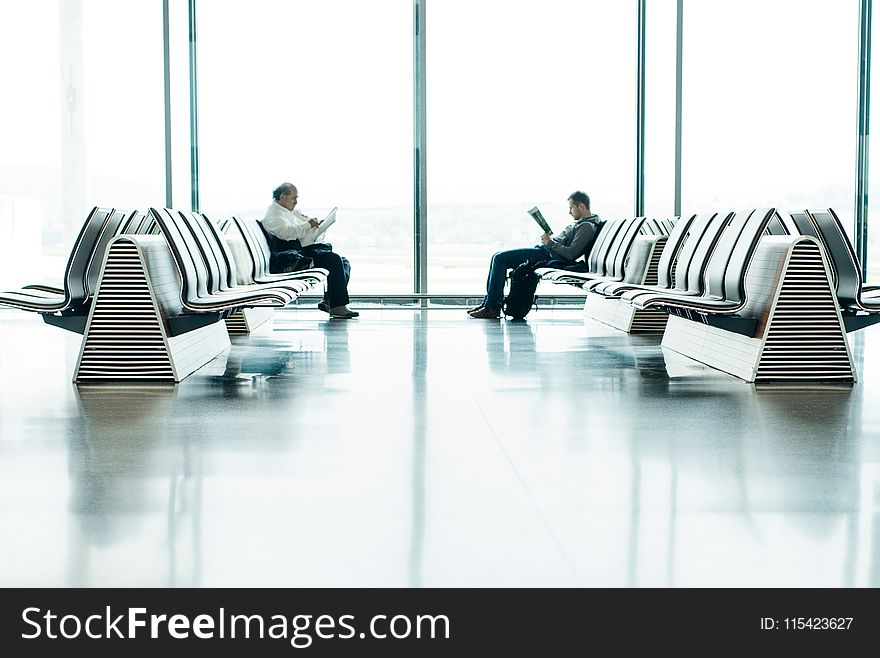 Two Men Sitting in Front of Each Other on White Gang Chairs in Airport Waiting Area