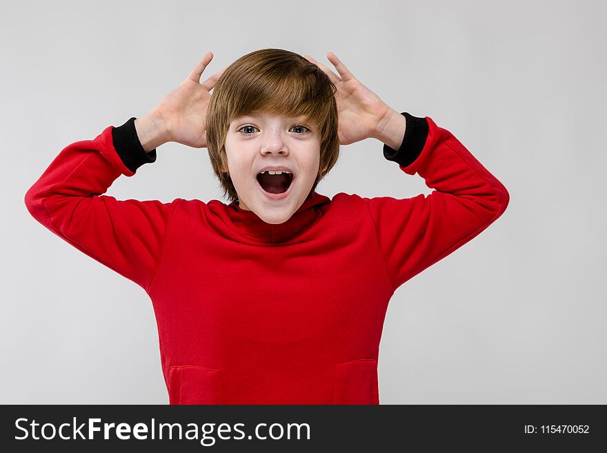 Portrait of cheerful little boy wearing red hoody and holding hands behind his head isolated on grey background with copyspace children`s fashion concept. Portrait of cheerful little boy wearing red hoody and holding hands behind his head isolated on grey background with copyspace children`s fashion concept.