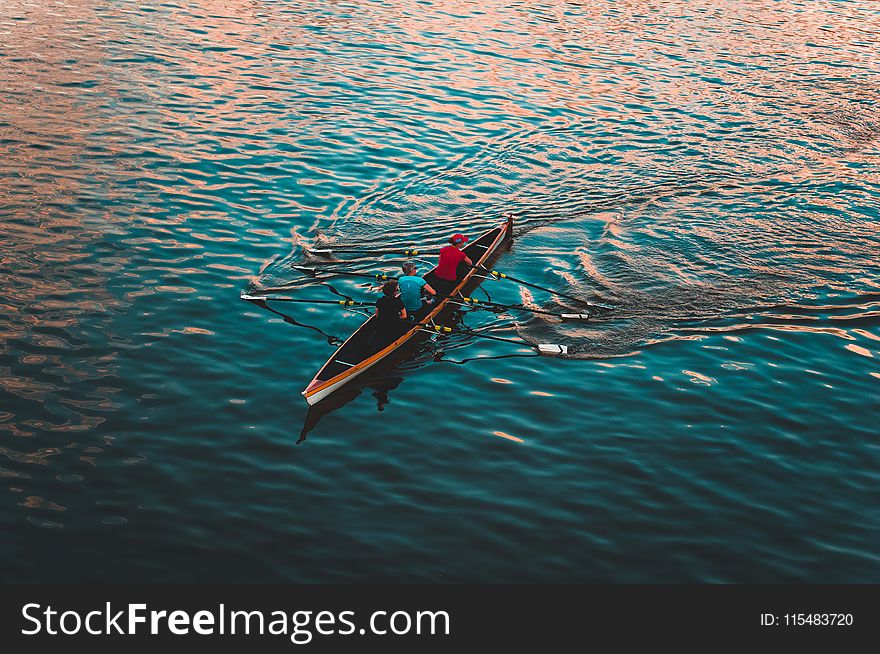 Three People on Brown Canoe Sailing on Calm Water