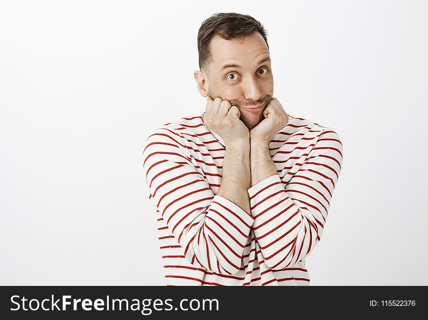 Indoor shot of cute emotive gay man in striped pullover, leaning face on palms and making tender duck face with pouting