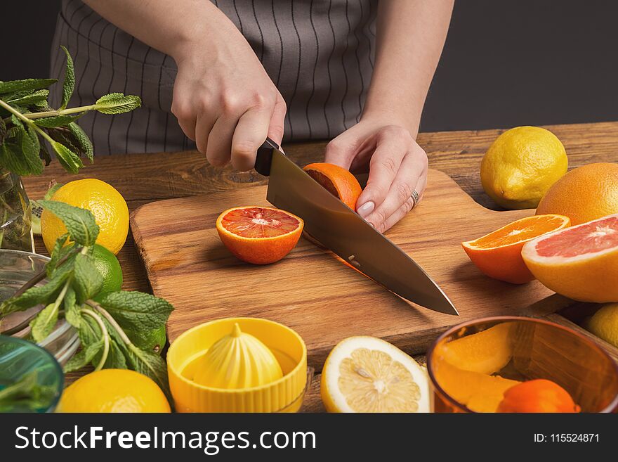 Female Hands Cutting Citrus Fruits On Wooden Board