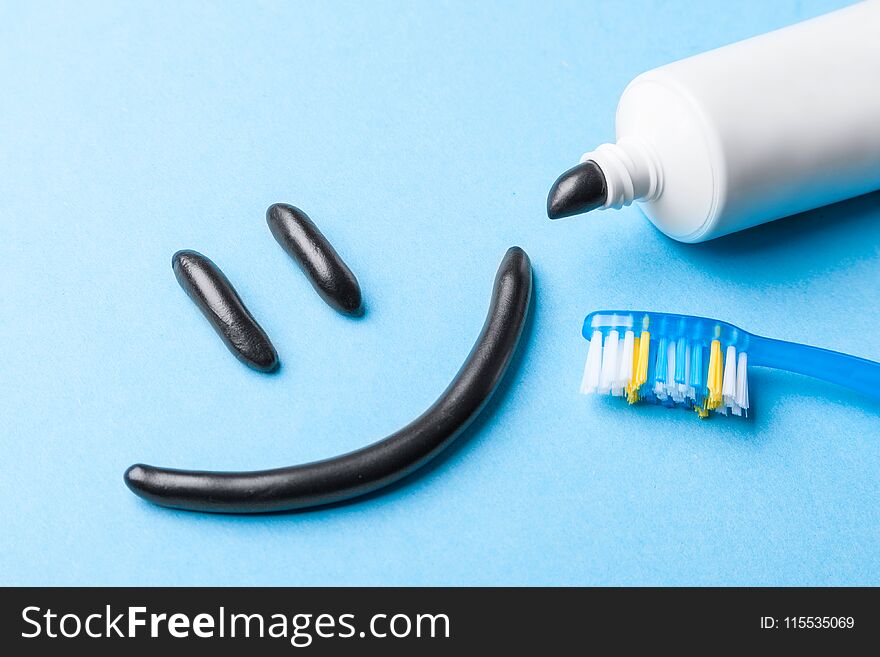 Black toothpaste from charcoal for white teeth. Toothpaste in the form of smile on the face, tube and toothbrush on blue