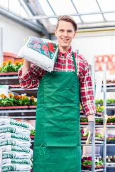 Cheerful Young Man Carrying A Bag Of Potting Soil While Working In A Flower Shop Stock Photography Cheerful Young Man Carrying A Bag Of Potting Soil While Working In A Flower Shop Stock Photography