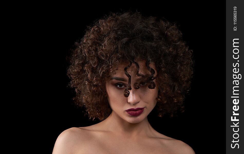 Exotic curly girl looking at camera and posing. Wearing light day make up with saturated violet lipstick. Having beatiful opened shoulders. Standing on black studio background. Exotic curly girl looking at camera and posing. Wearing light day make up with saturated violet lipstick. Having beatiful opened shoulders. Standing on black studio background.