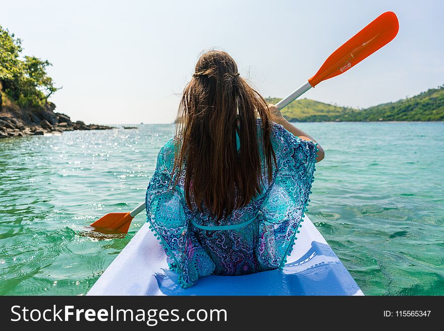 Rear view of a young woman with long brown chestnut hair paddling a canoe along the shore of an idyllic island during vacation in Indonesia. Rear view of a young woman with long brown chestnut hair paddling a canoe along the shore of an idyllic island during vacation in Indonesia