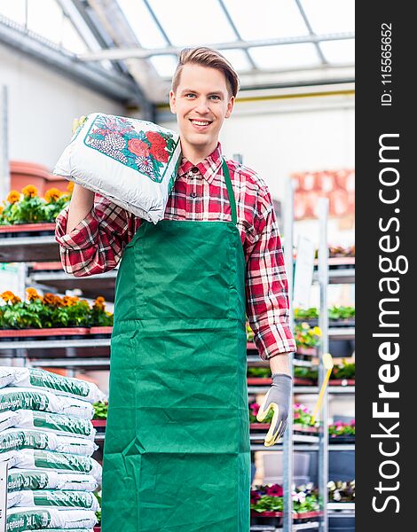 Portrait of a cheerful young man carrying a bag of high-quality potting soil while working as floristry specialist in a modern flower shop. Portrait of a cheerful young man carrying a bag of high-quality potting soil while working as floristry specialist in a modern flower shop