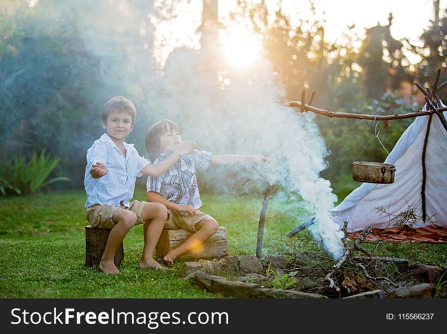 Two sweet children, boy brothers, camping outside summertime on sunset, eating potatoes