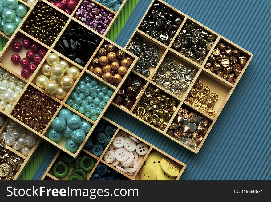 Different clothes buttons in wooden boxes on green and blue cardboard background.