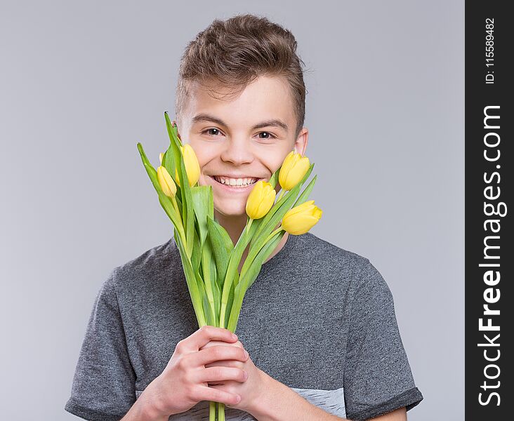 Teen boy with bunch of flowers on gray background. Smiling child with bouquet of tulips as a gift. Happy mothers, Birthday or Valentines day. Teen boy with bunch of flowers on gray background. Smiling child with bouquet of tulips as a gift. Happy mothers, Birthday or Valentines day.