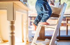 Toddler Boy In A Dangerous At Home, Climbing Into Highchair. Stock Photo