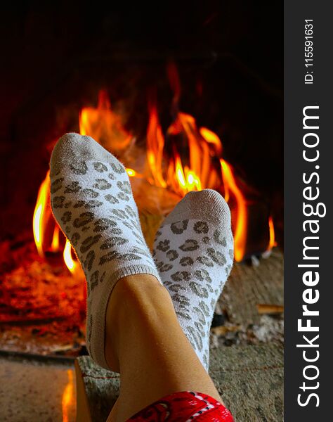 Burning Wood At The Fireplace, Female Legs In Socks Warming Up.