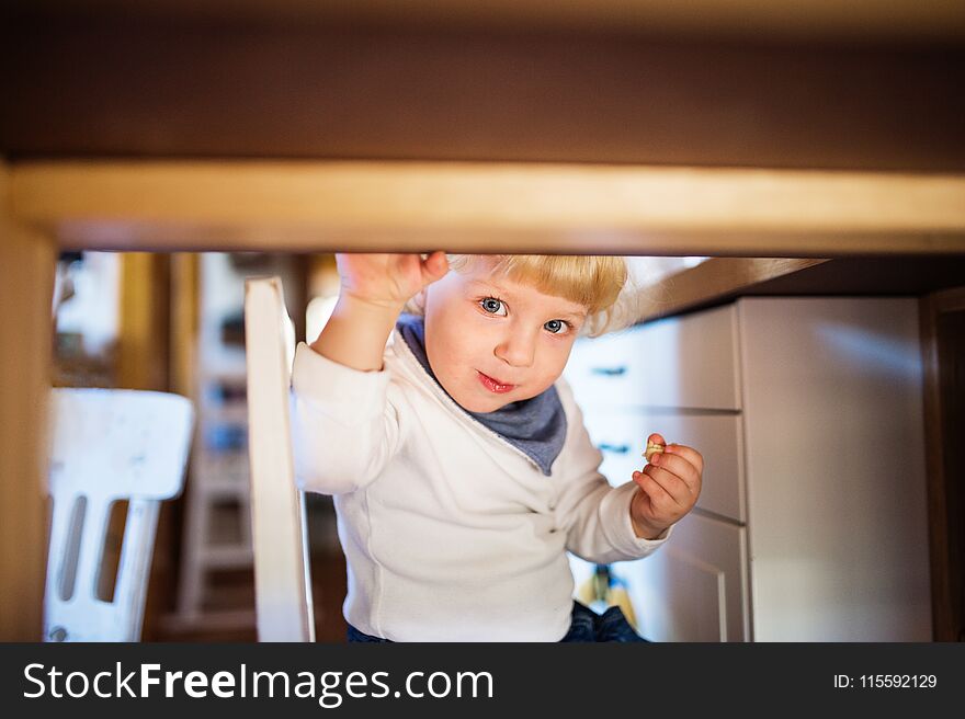 Cute toddler boy eating sweets under the table. Child safety concept.