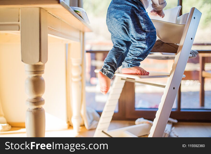 Little toddler boy climbing on wooden highchair at home. Domestic accident. Dangerous situation at home. Little toddler boy climbing on wooden highchair at home. Domestic accident. Dangerous situation at home.