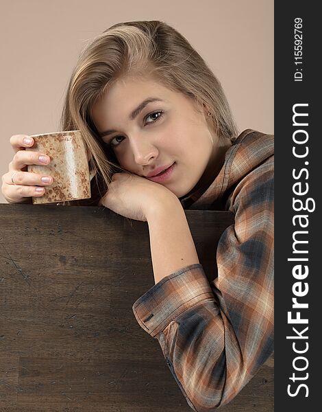 Young pretty blonde woman in brown plaid shirt with coffee mug . Old wooden bacground , copy space for your text.