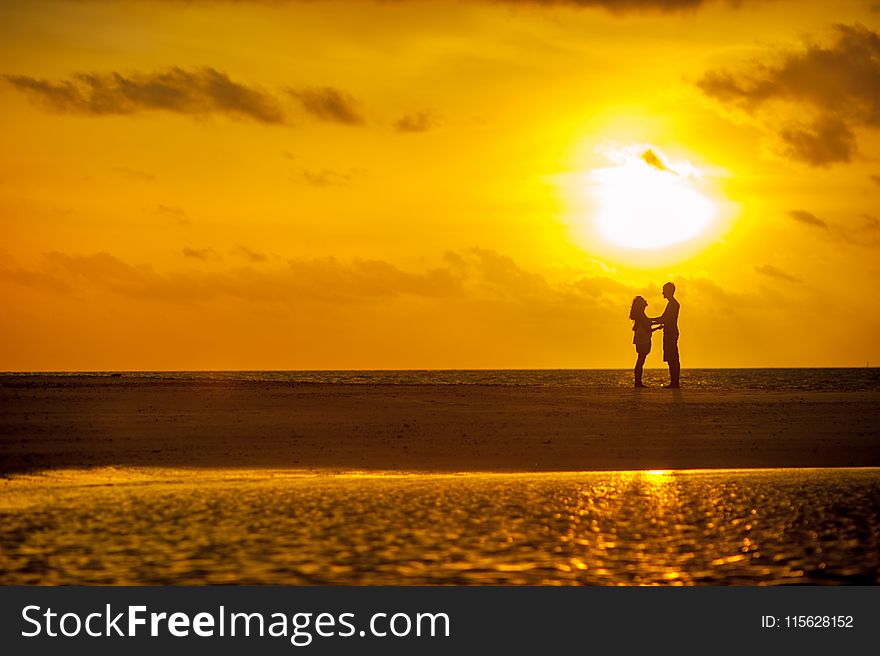 Man and Woman Standing Near Seashore Under Sunset