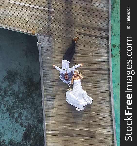 Photo of Bride and Groom Laying on Pier