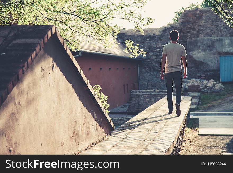 Man Wearing Gray T-shirt and Black Denim Jeans Walking Towards Gray Concrete Pathway