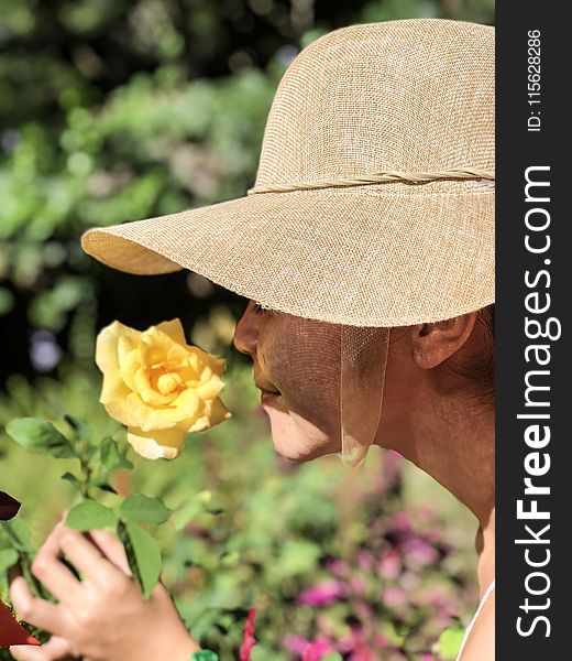 Woman Wearing Sun Hat Smelling Yellow Rose