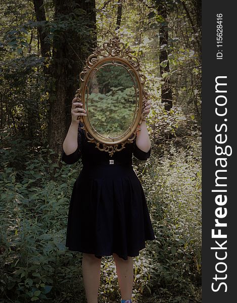 Woman Holding Mirror Against Her Head in the Middle of Forest